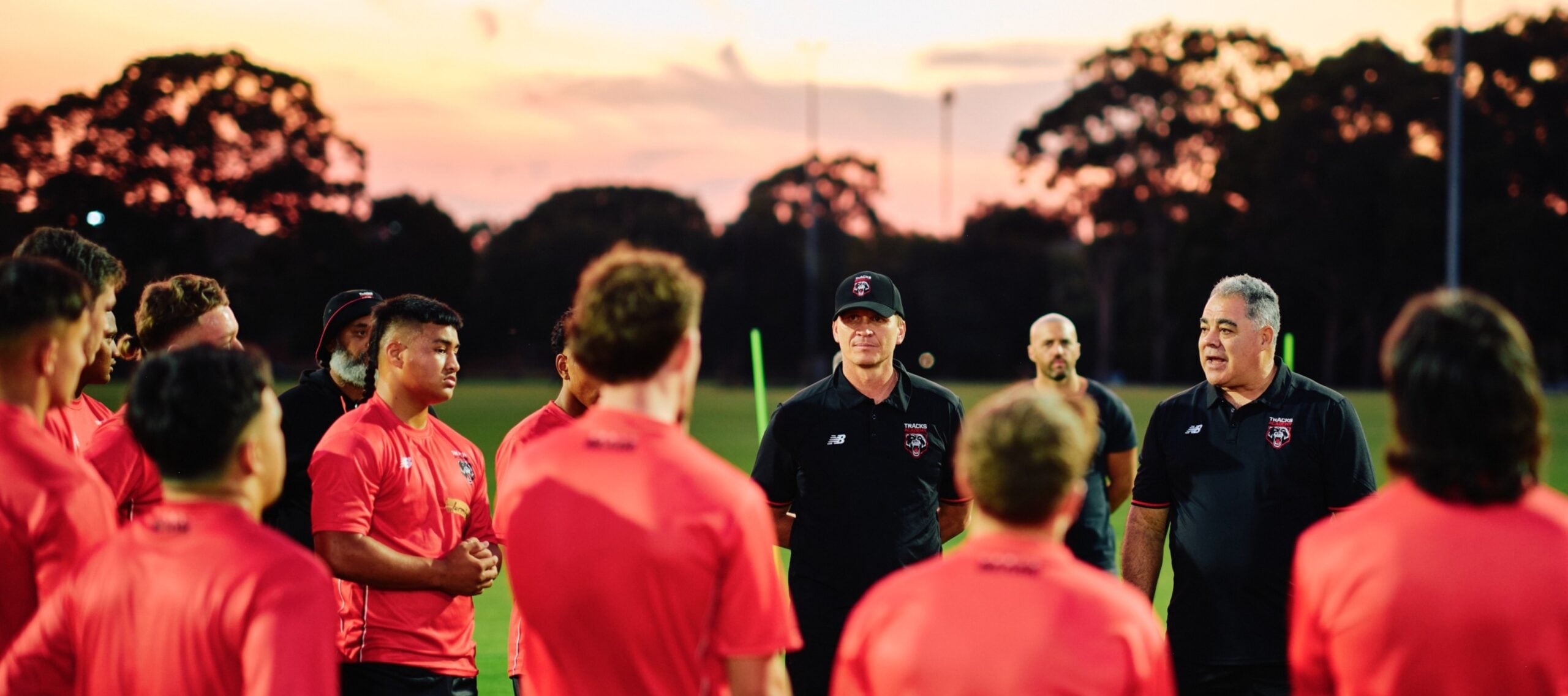 Image of Head Coach, Mal Meninga, and assistant coach, Ben Gardiner, working with Tracks academy players whose backs are to camera